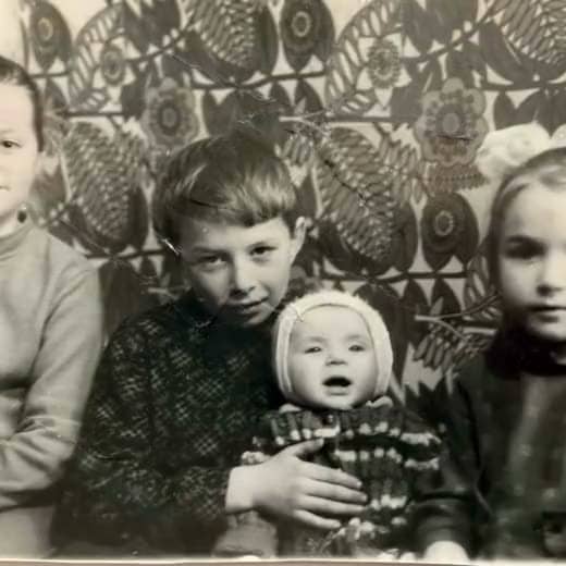 Мальчик держит младенца, рядом две девочки, за ними ковёр с узором